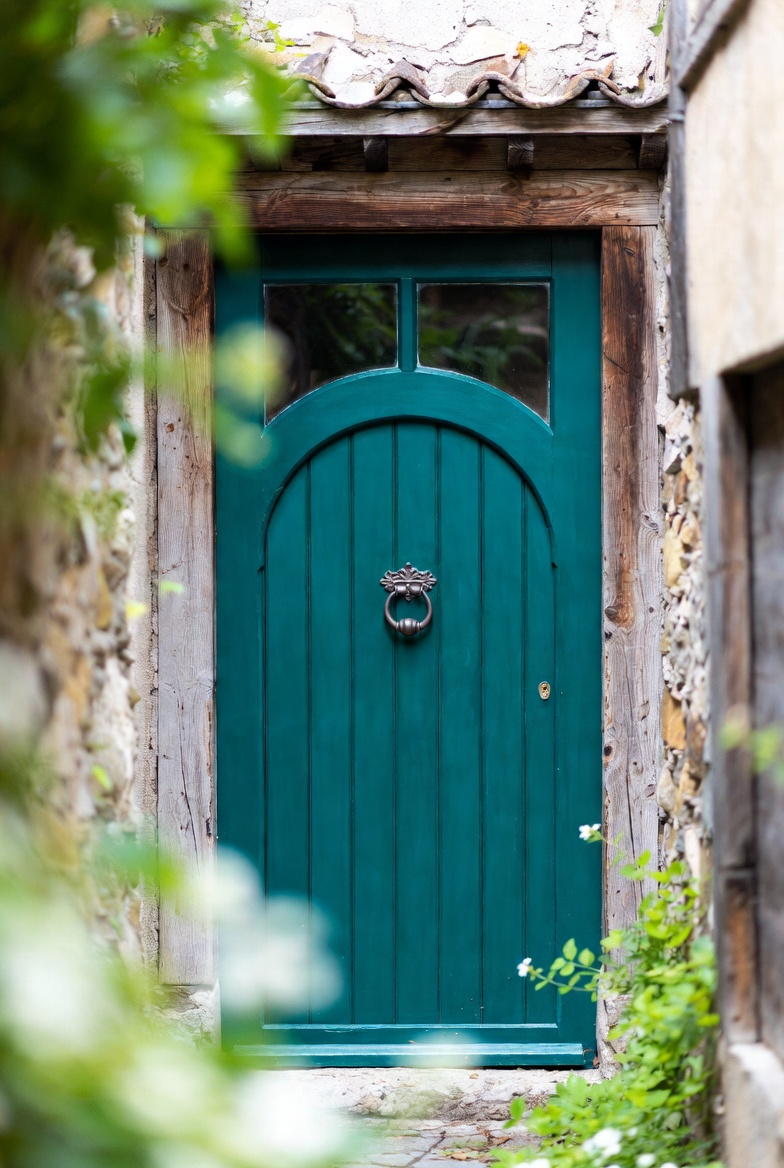 A teal wooden front door set in a stone wall with greenery.