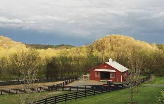 A red barn and black board fence beneath spring hills and a storm-lit sky
