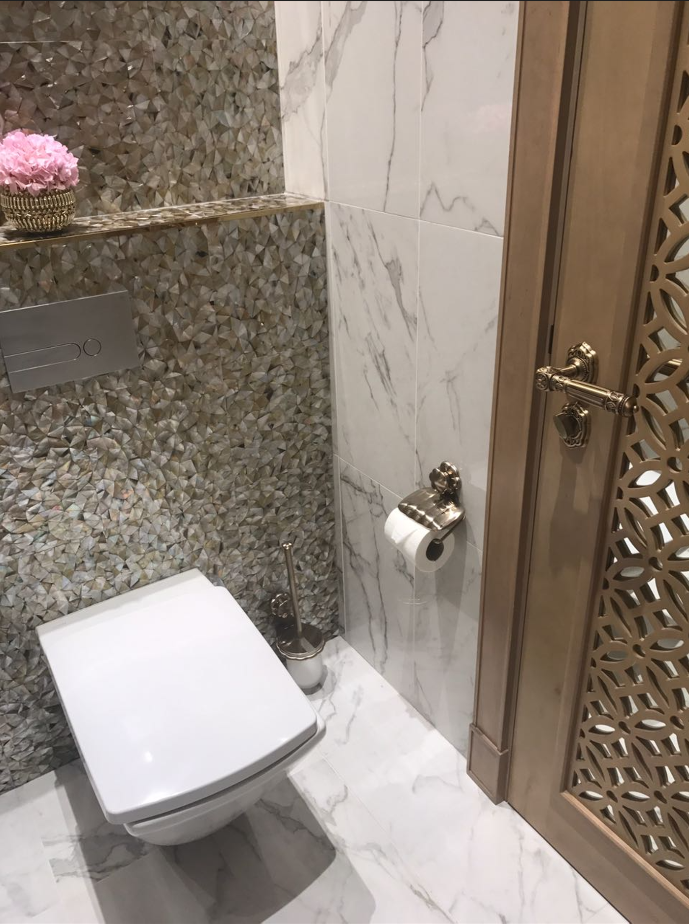 Luxury bathroom, marble walls and custom wooden doors. Bother of pearl lines the back wall, with pink flower in a golden vas
