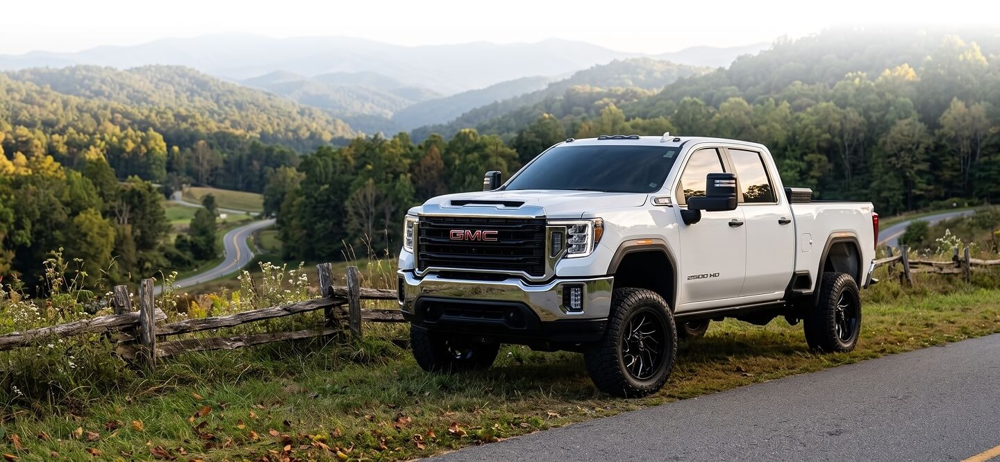 Lifted white GMC Sierra HD pickup parked on a mountain road