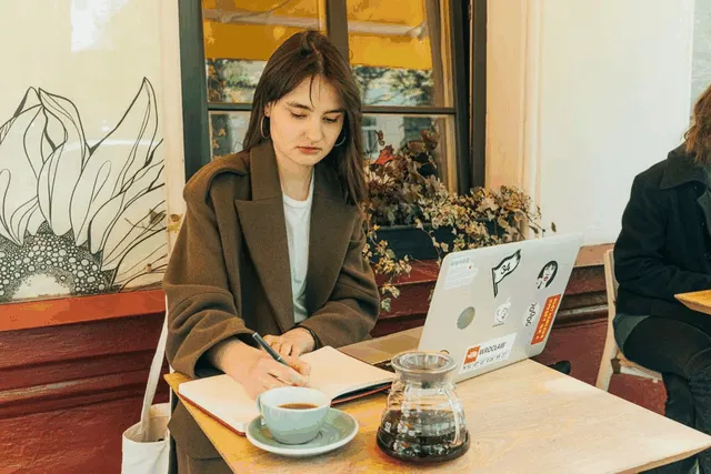 A café owner taking notes beside a laptop and coffee
