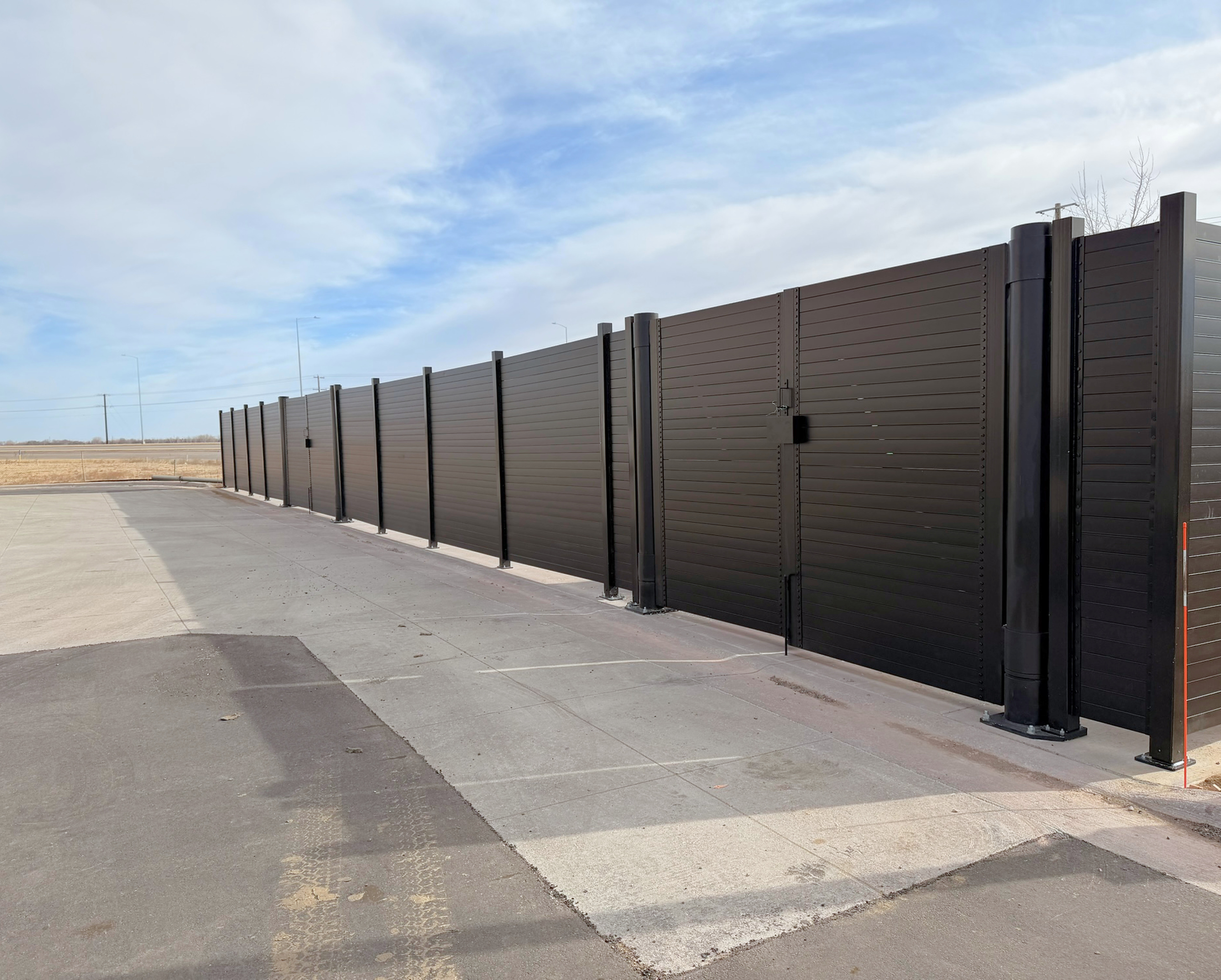 Long run of 8 ft Alpine Citadel structural steel screen wall with a double-leaf gate on round gate posts