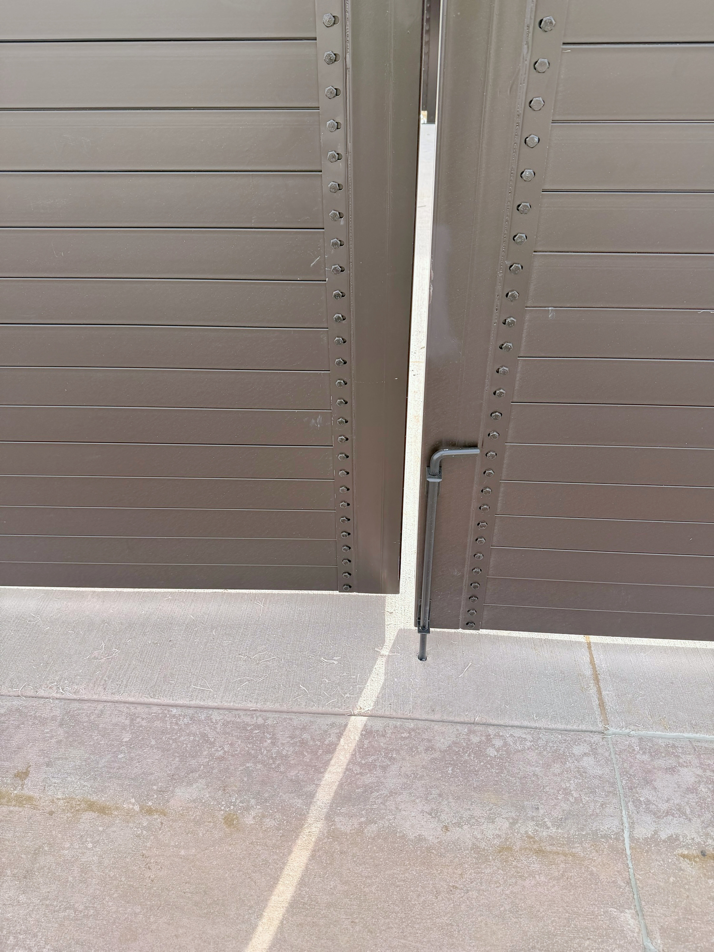 Cane bolt on a 12 ft clear double-leaf steel gate dropped into its slab sleeve