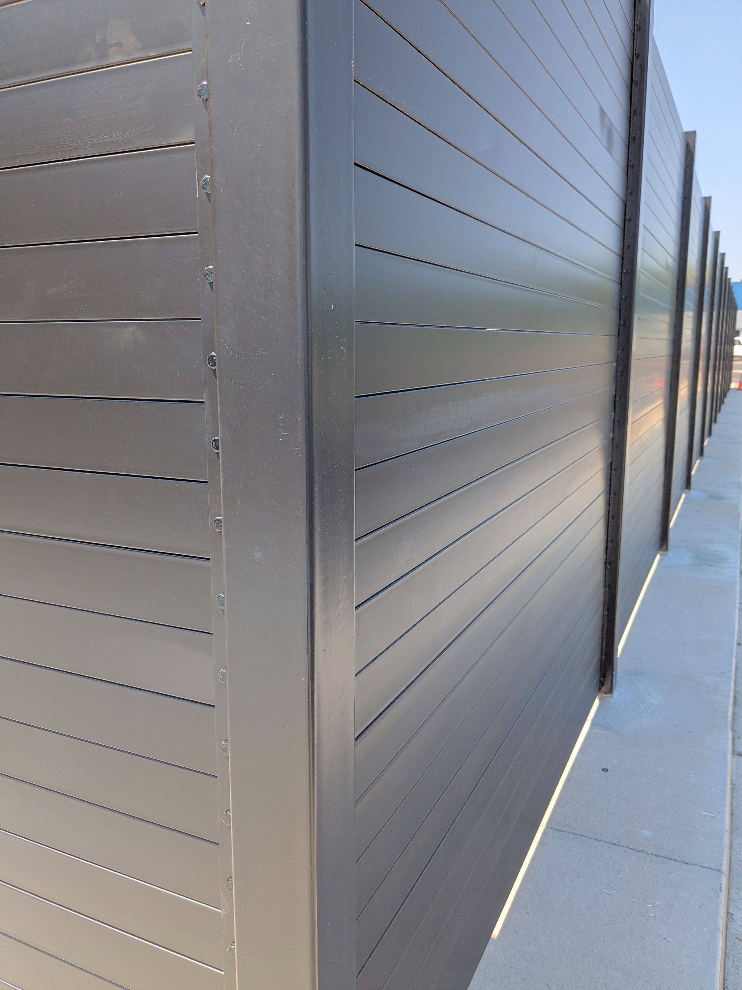 Solid steel slats stacked in a structural steel post channel at an enclosure corner