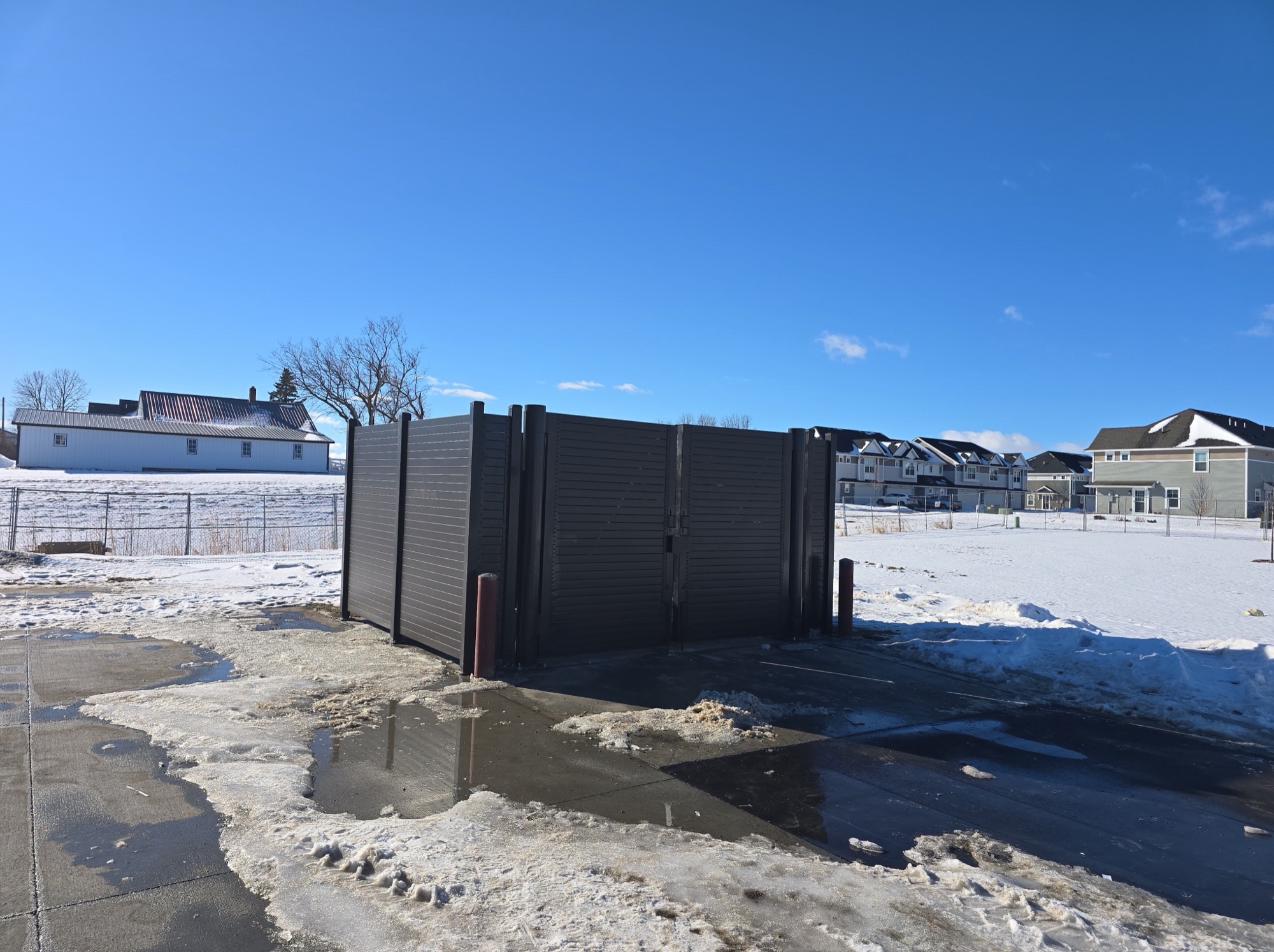 Structural steel trash and tire storage enclosures with double-leaf gates and bollards at a tire and automotive service center