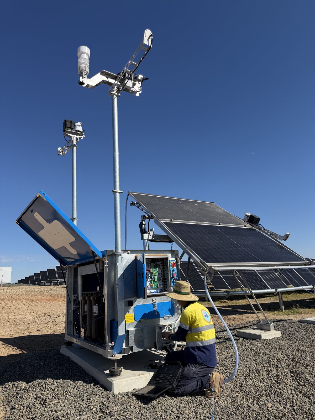 Technician servicing an open weather station enclosure beside reference solar modules
