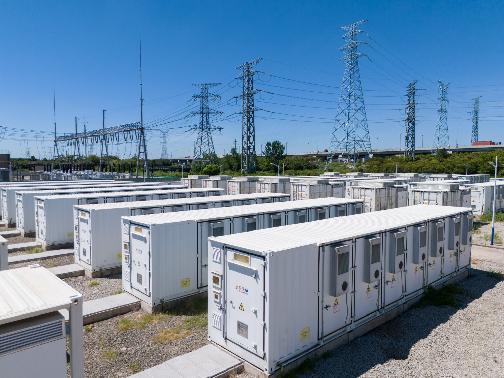 Rows of battery storage containers beside high-voltage transmission towers