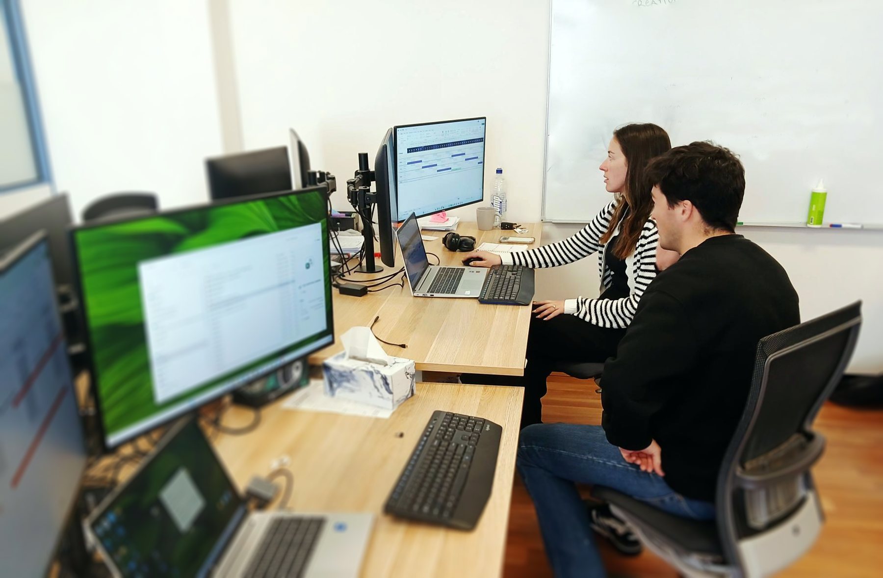 Two Proa team members working together at a desk with multiple monitors