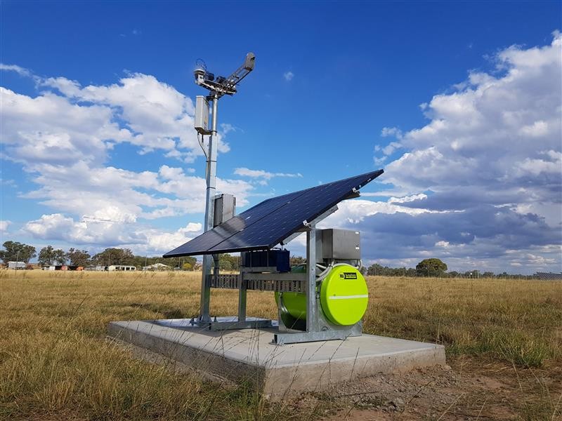 Standalone MetEdge with solar panel, cleaning water tank and sensor mast on a concrete pad in a grassy field