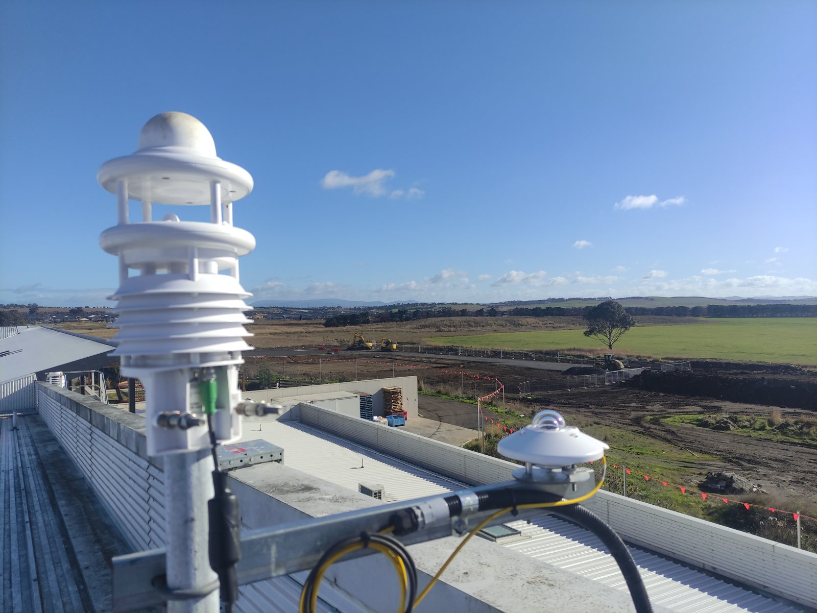 MetLite compact weather sensor and pyranometer on a rooftop mast overlooking a construction site