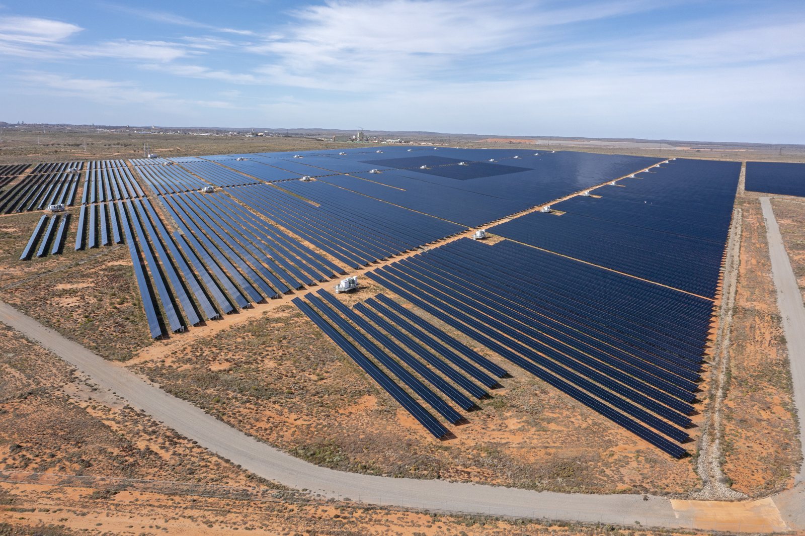 Aerial view of a large solar farm with rows of tracker panels in red desert country