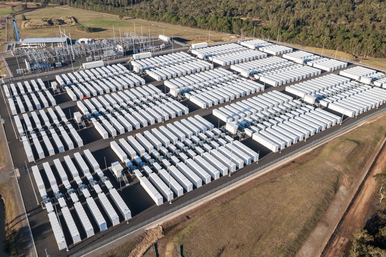 Aerial view of a large battery energy storage system with rows of battery enclosures beside a substation