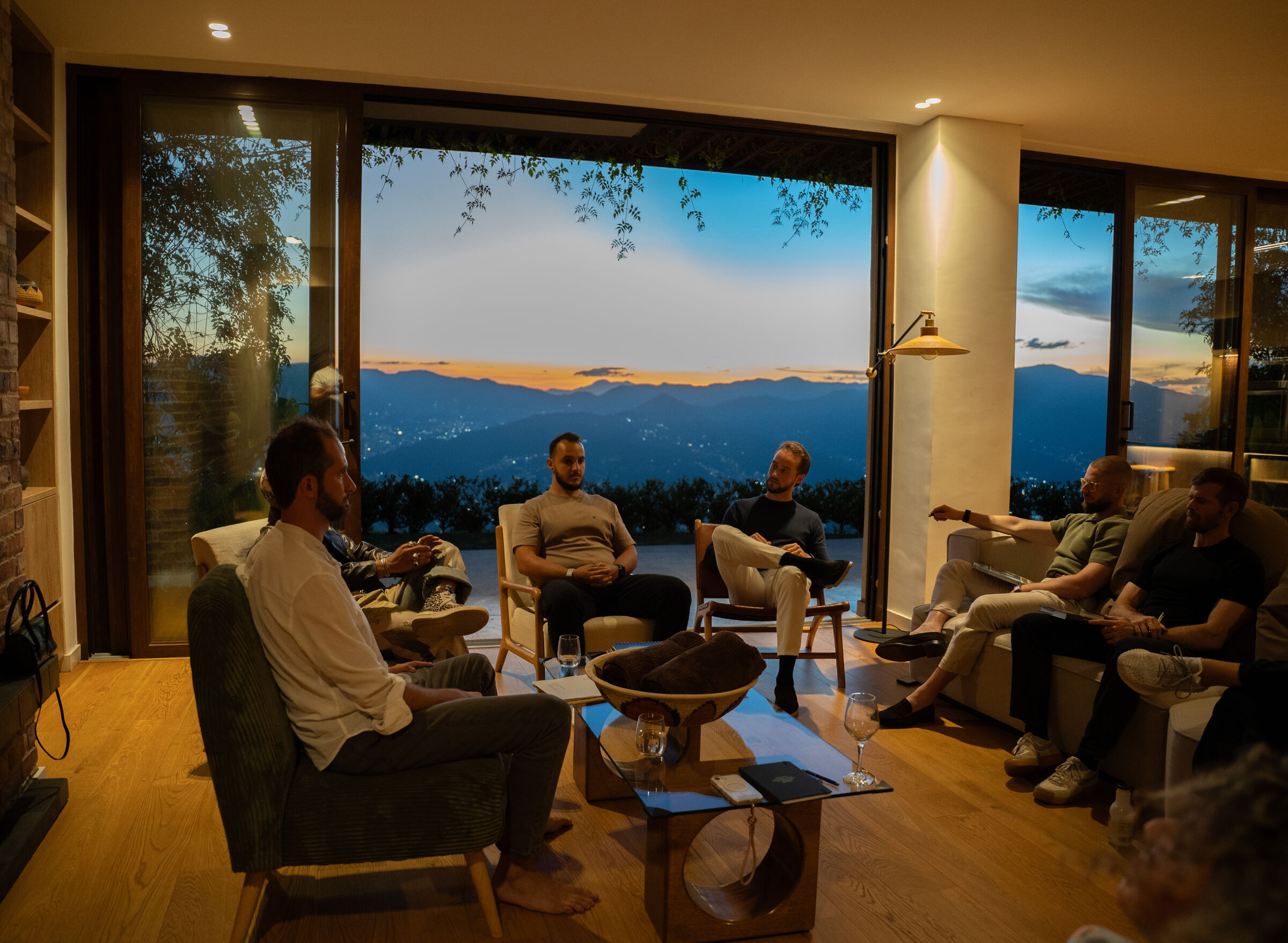 Founders seated in a circle of armchairs in conversation, in front of a window at sunset over the mountains.