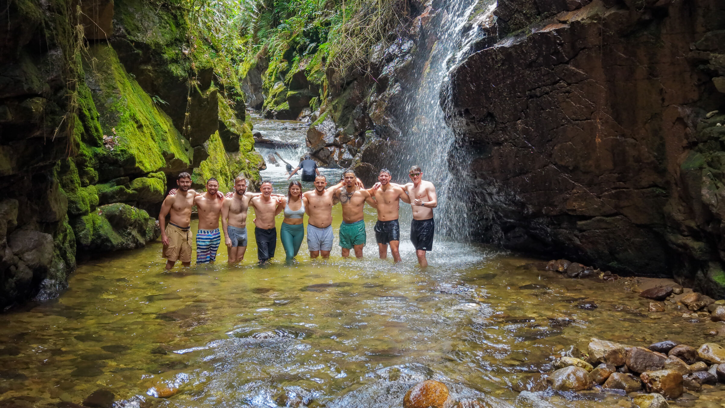 Founders Reset attendees standing together in a river pool at the foot of a waterfall.