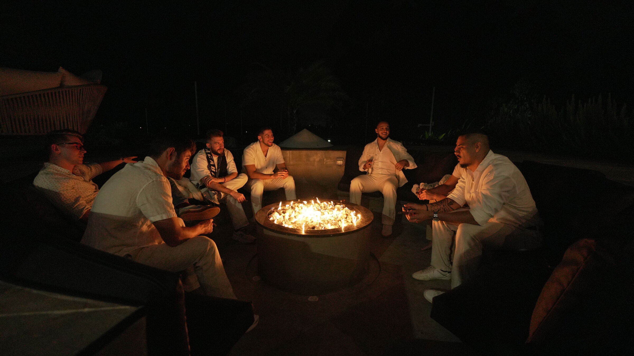Founders Reset attendees in white seated around a fire pit at night.