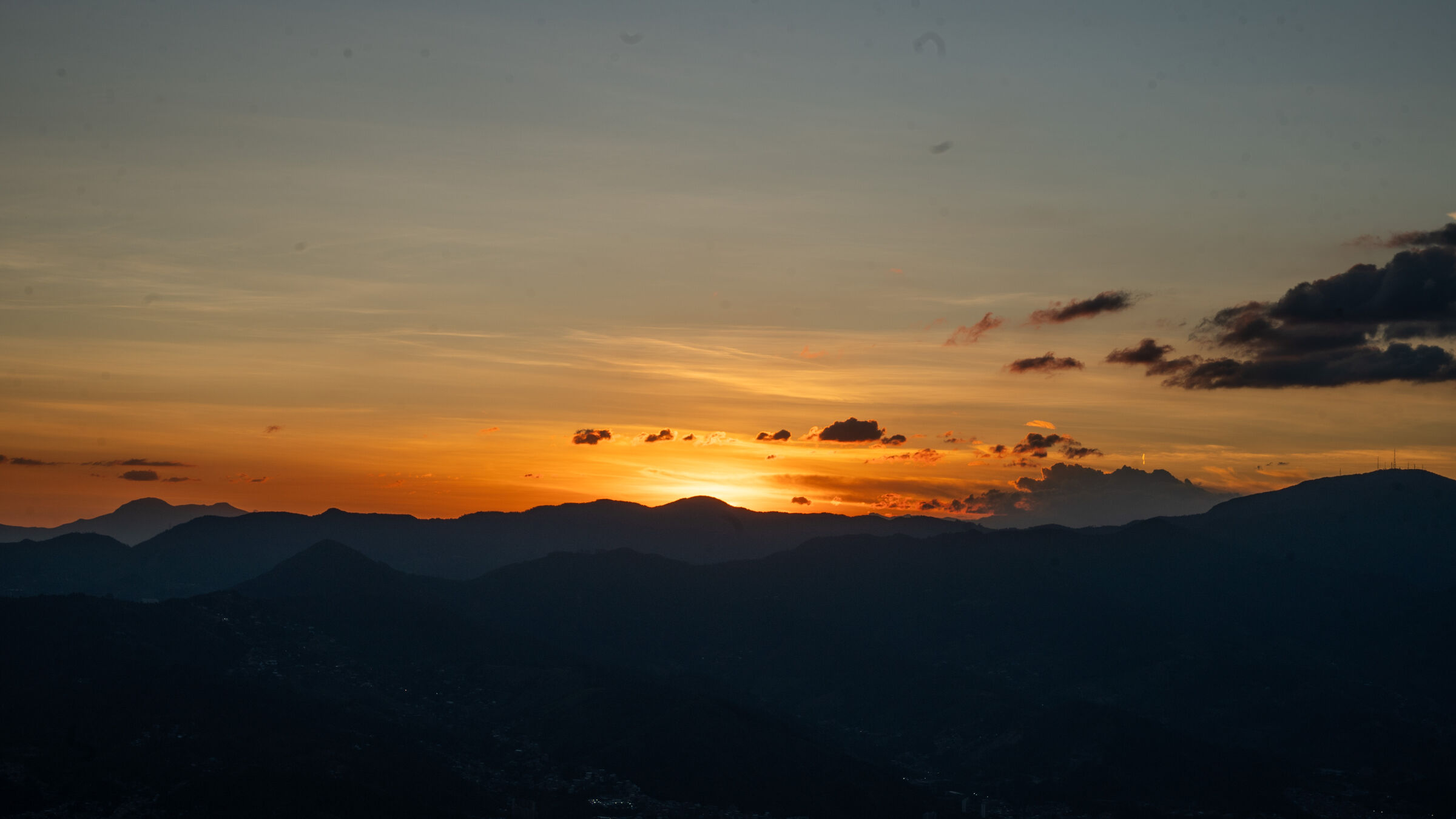 The sun setting behind a mountain ridgeline under a streaked sky.