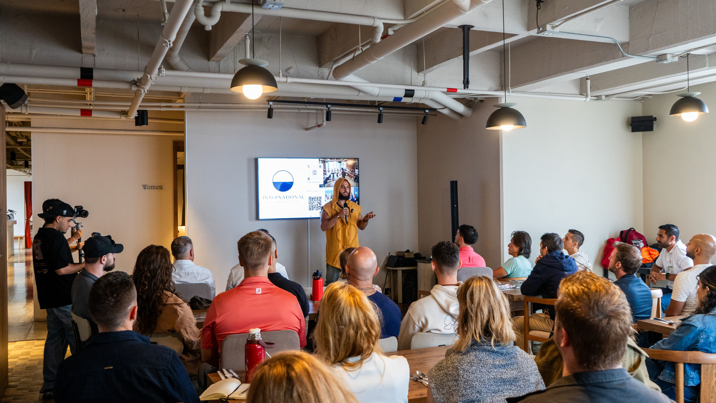 A speaker presenting to a seated room at an International Breakfast Club gathering.