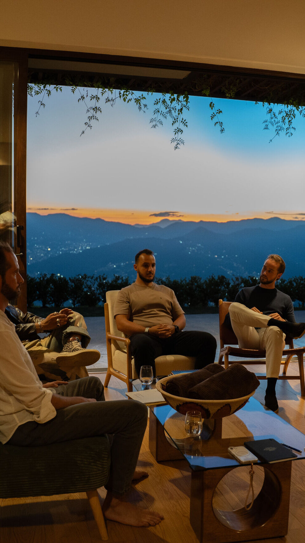 Founders seated in a circle of armchairs in conversation, in front of a window at sunset over the mountains.