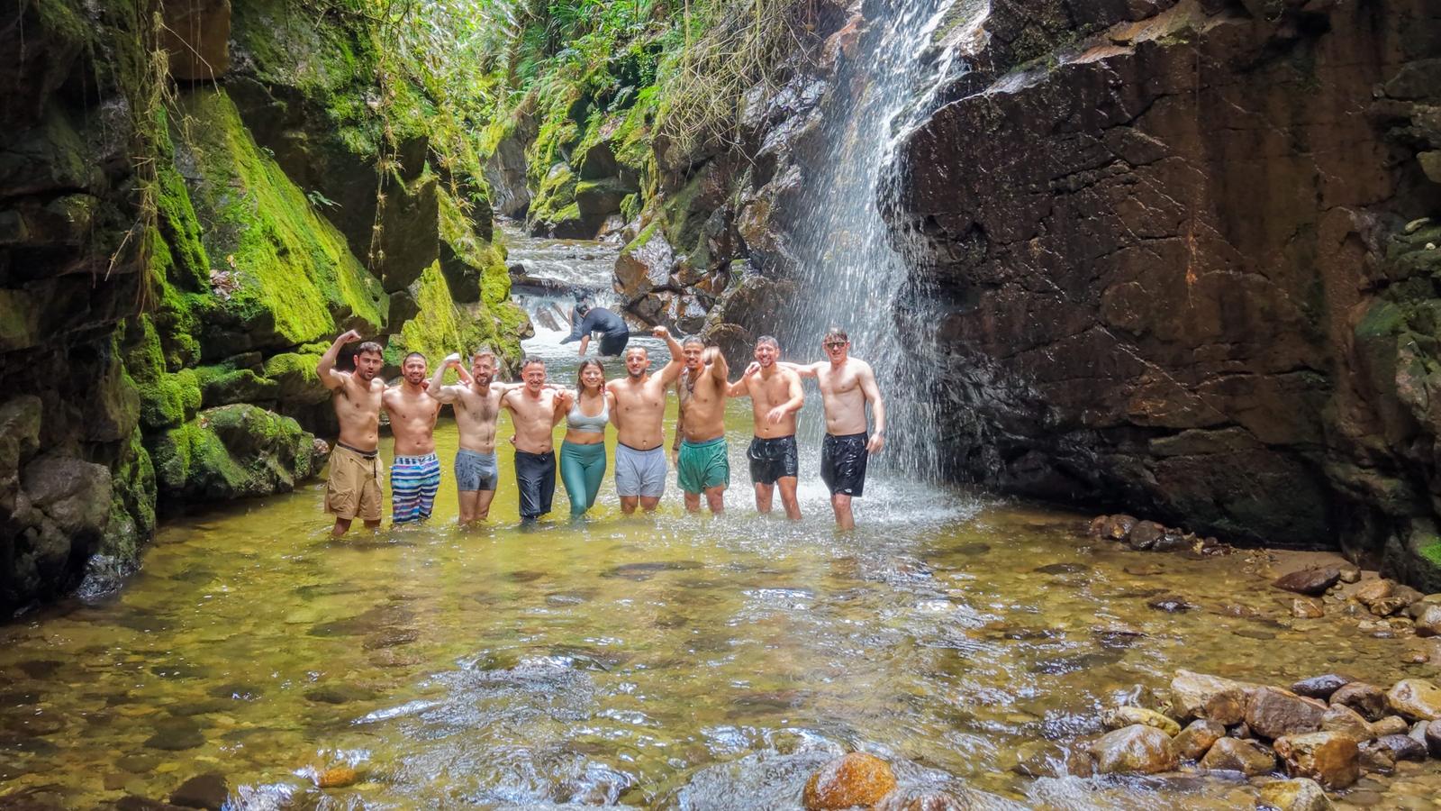 Founders Reset attendees arm in arm in a river pool below a waterfall.