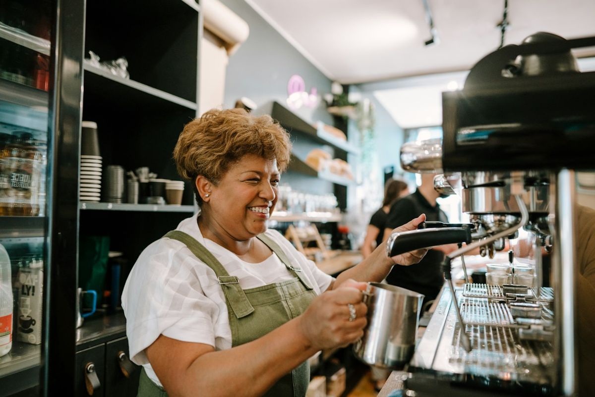 Café worker smiling while steaming milk at the coffee machine