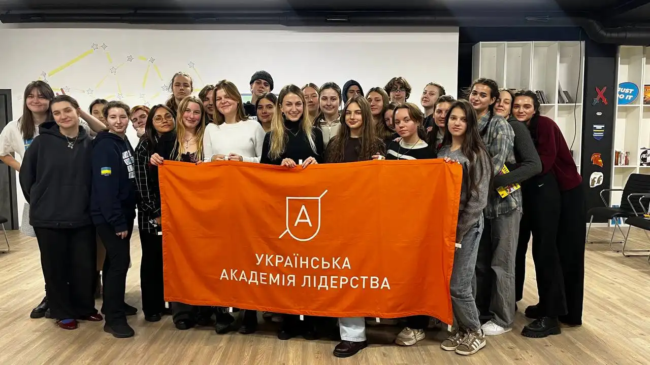 Group of young people standing indoors holding an orange banner with a white logo and Ukrainian text reading 'Українська Академія Лідерства' (Ukrainian Leadership Academy).