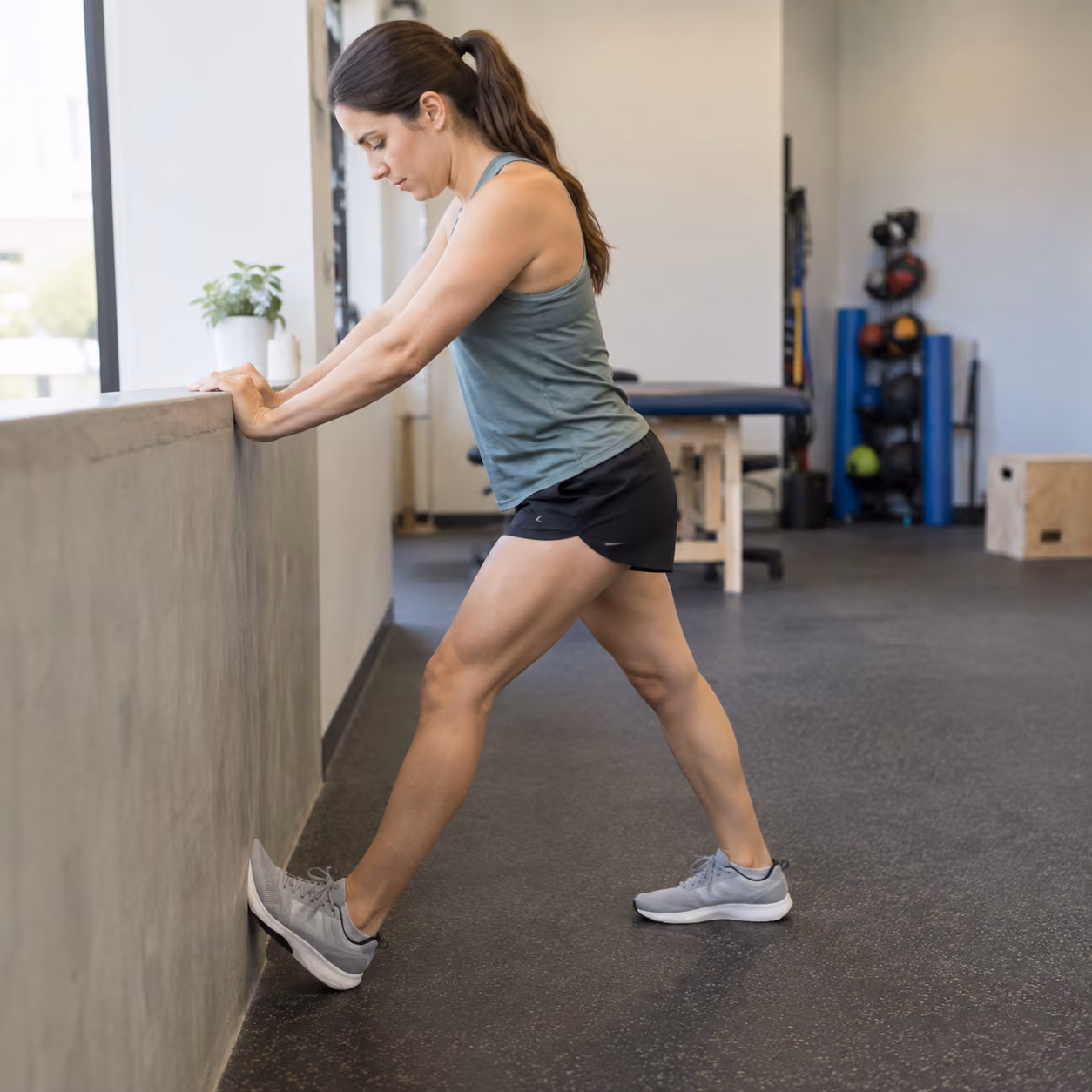 Woman performing a calf mobility stretch against a wall in a rehabilitation studio.