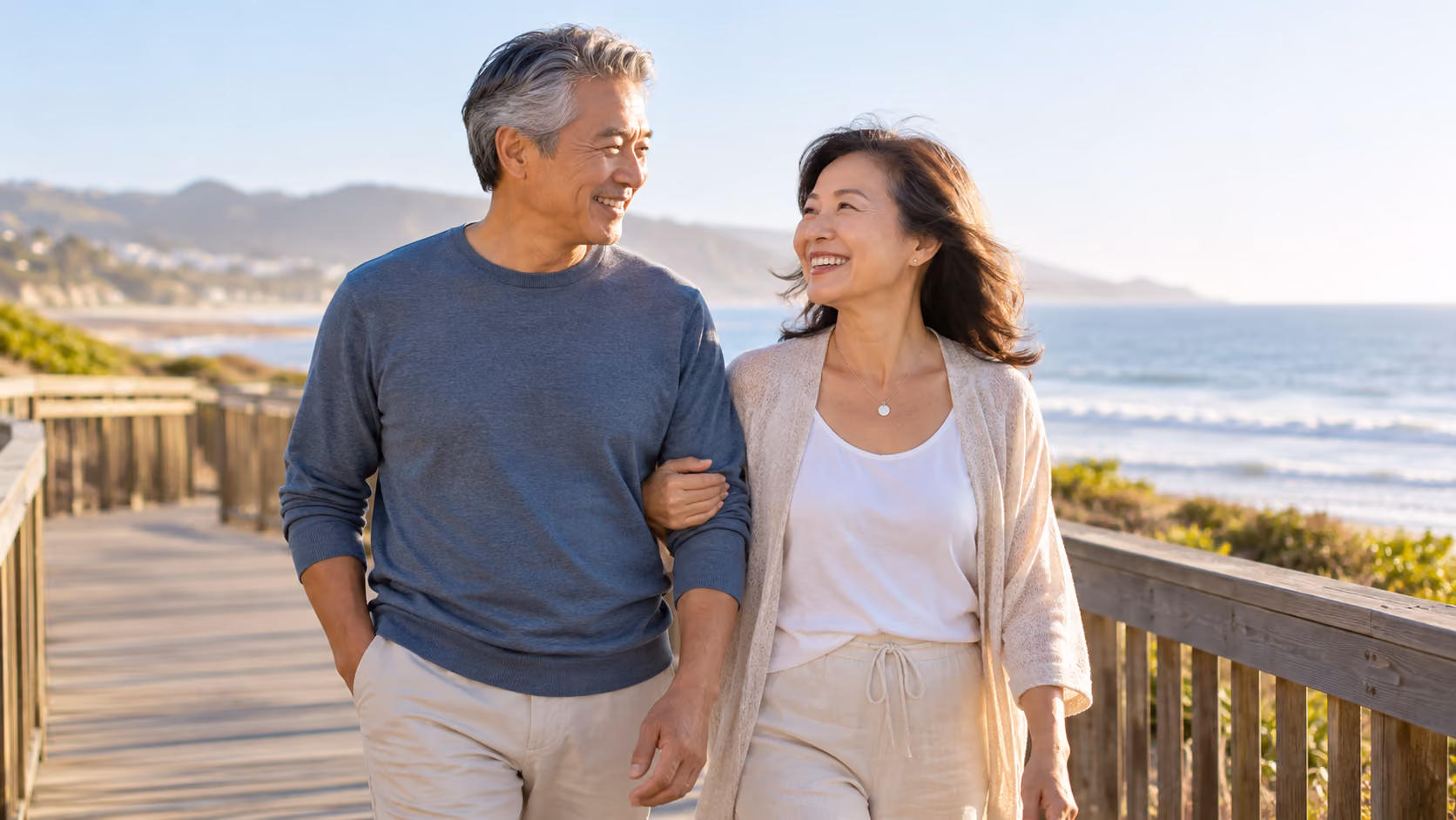 Older couple walking together along a coastal boardwalk.