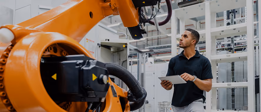 Engineer with a tablet inspecting an orange industrial robot arm
