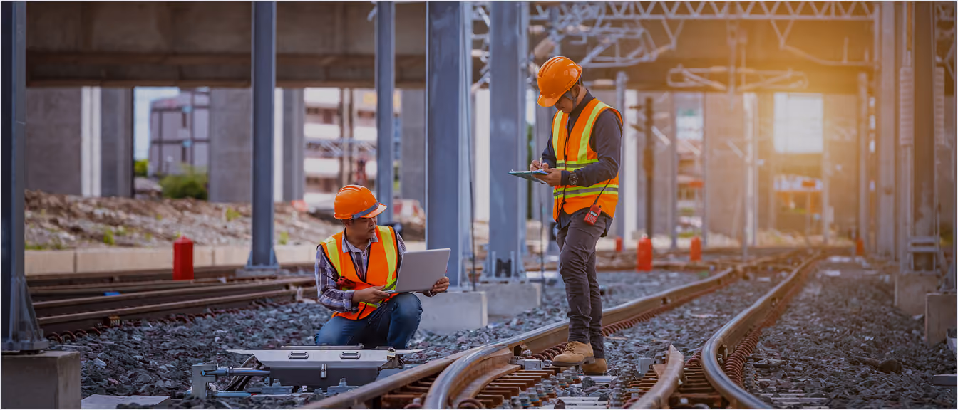 Rail engineers in hard hats and safety vests checking equipment on railway tracks