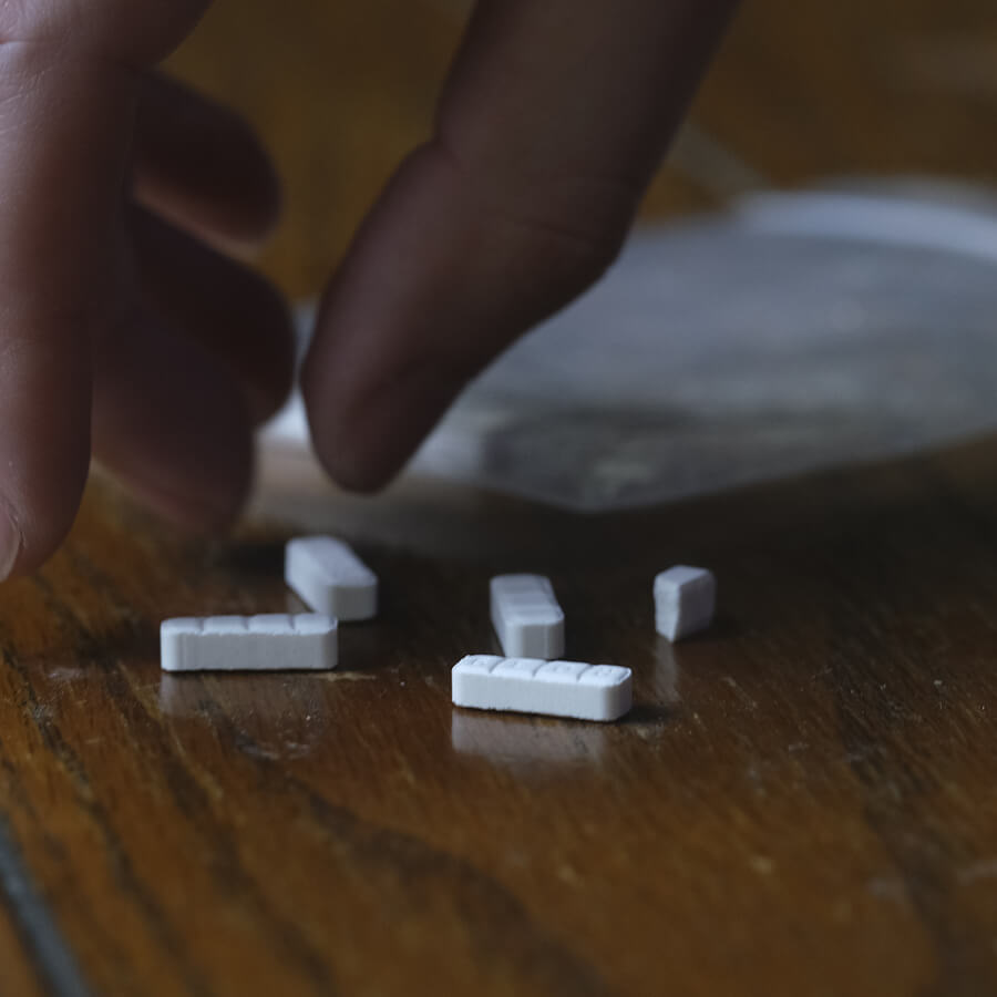 White bar shaped pills with hand reaching to grab them