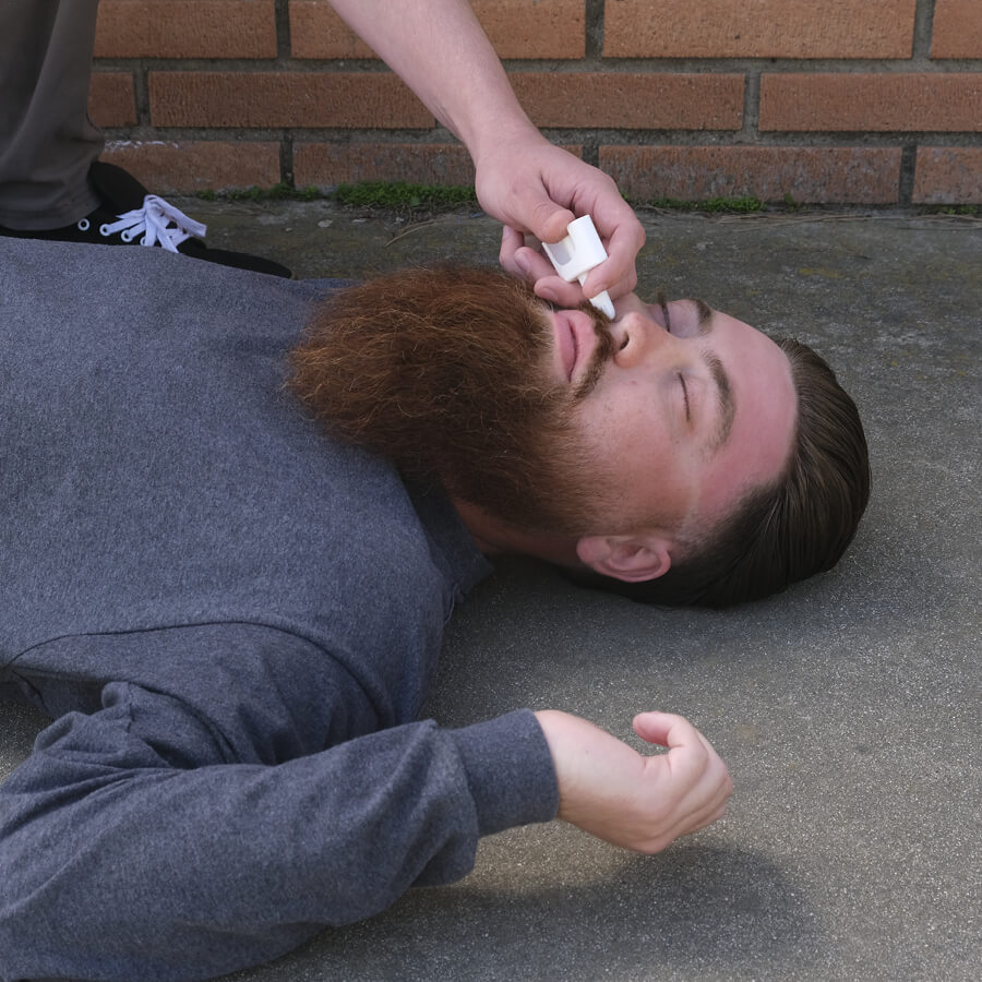 Man passed out on sidewalk, with a second person administering naloxone in nose