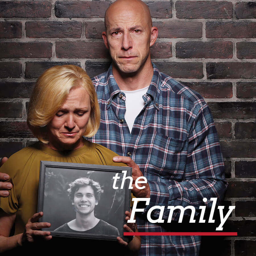 A mother and a father holding a photograph of their son, looking sad