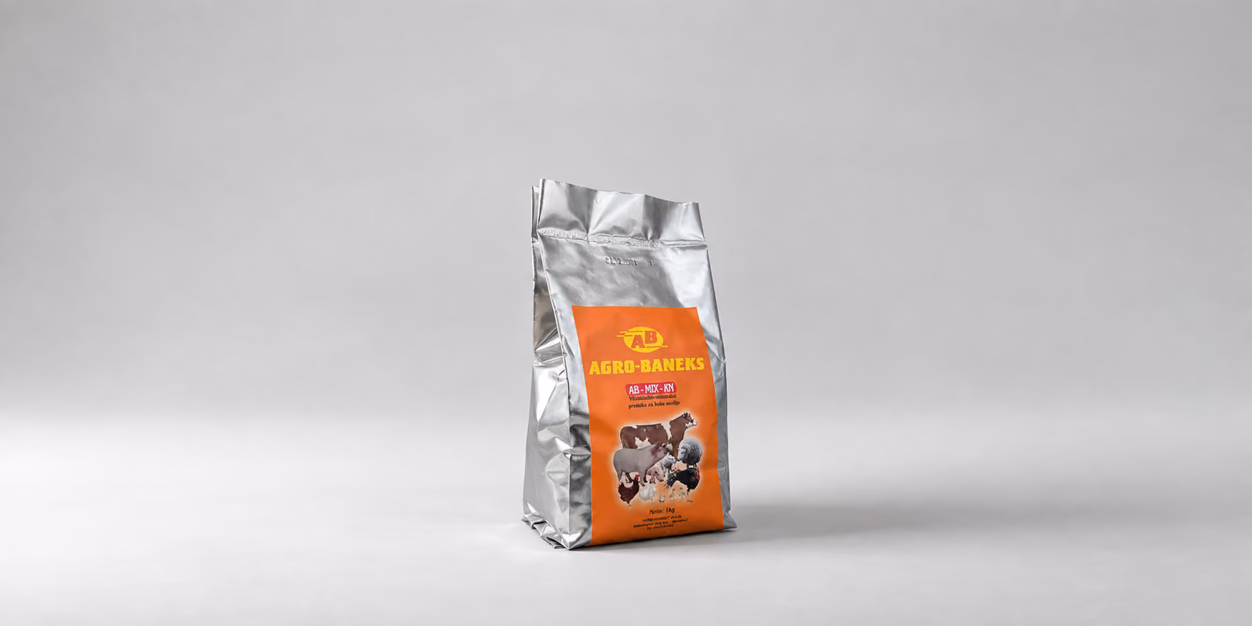 Silver bag of Agro-Baneks animal feed with an orange label showing images of cows and chickens against a plain gray background.