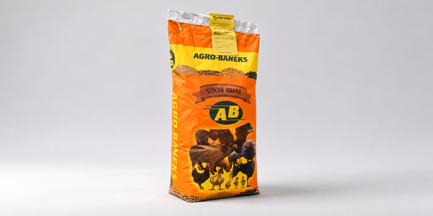 A tall orange and yellow bag of animal feed labeled AGRO-BANEKS with images of a cow, pig, sheep, chicken, and chicks on the front.