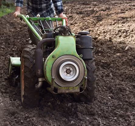 Person operating a green rotary tiller machine on freshly plowed soil outdoors.