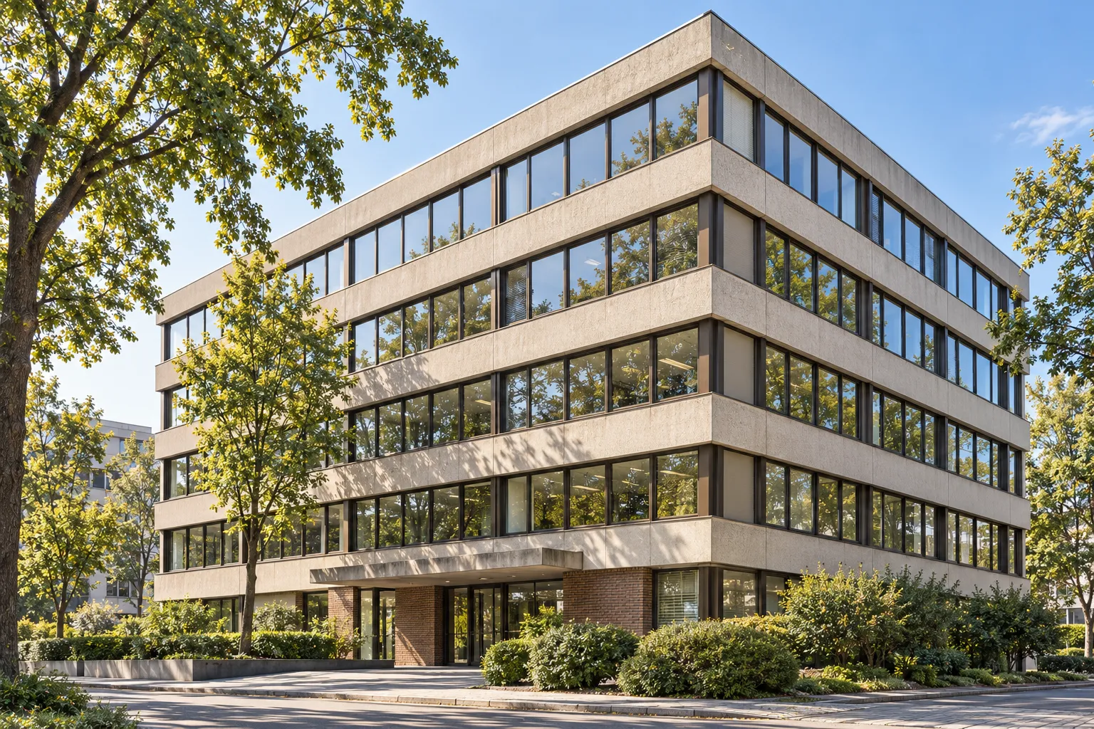 Gepflegtes Bürogebäude im Bestand mit älterer Betonfassade und gewachsenem Baumbestand.