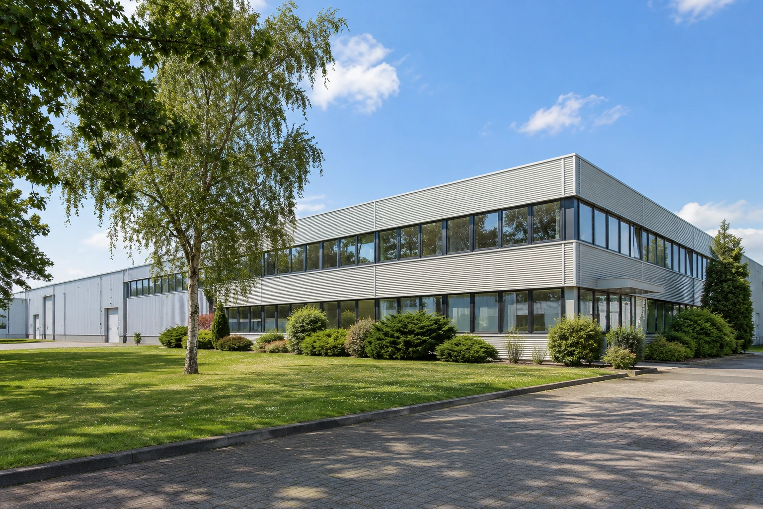 Bestehendes Gewerbegebäude mit heller Fassade und gewachsenen Bäumen.