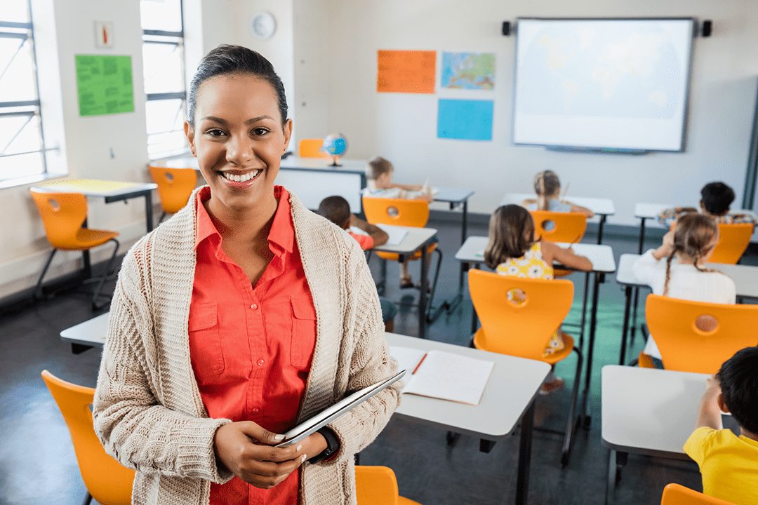 Teacher holding a tablet at the front of a classroom of students