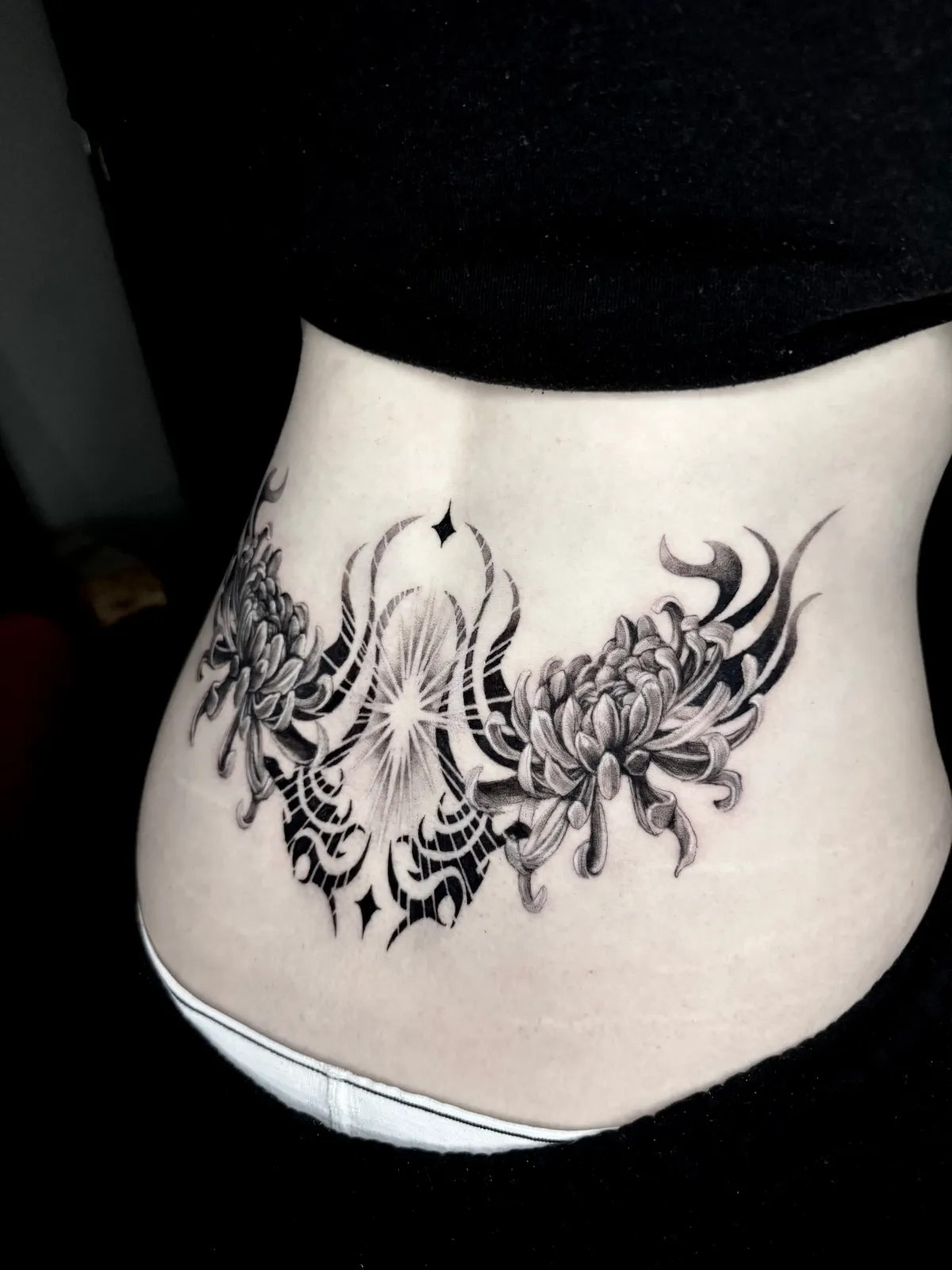 Blackwork chrysanthemum and ornamental lower back tattoo by Sora at SANS PATRIE/ STUDIO