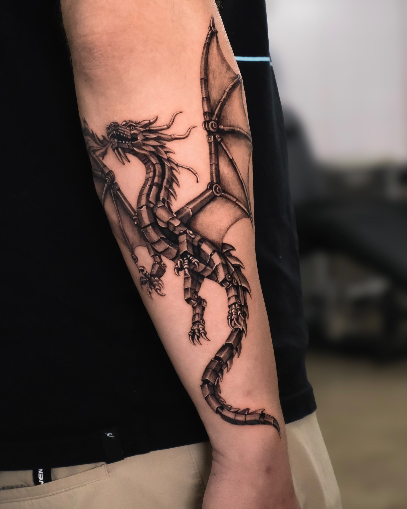 Black and grey mechanical dragon forearm tattoo by Ruth Bitton at SANS PATRIE/ STUDIO