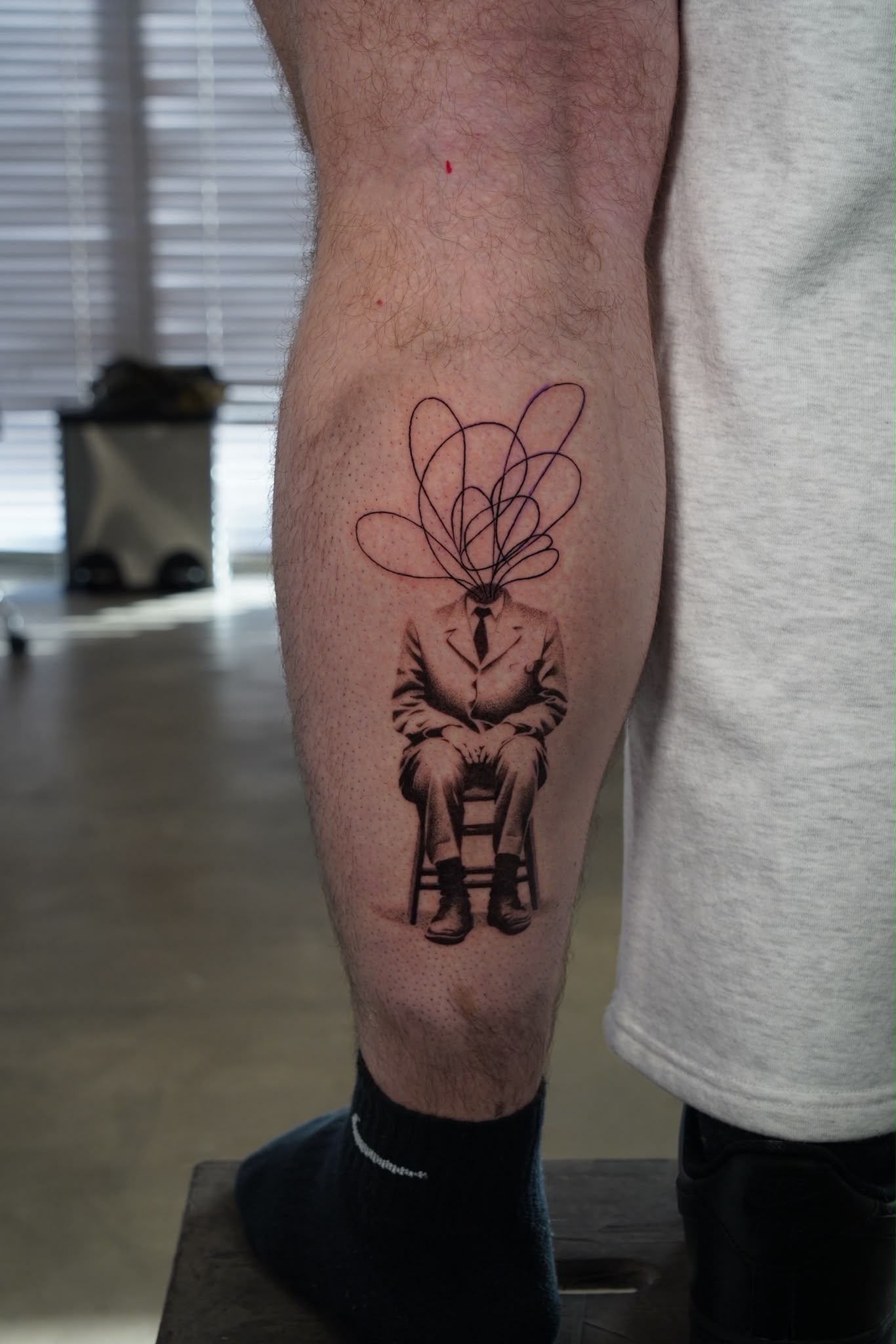 Surreal fine line tattoo of a seated figure with a scribbled head, on the calf, by Tyrese Gilzene at SANS PATRIE/ STUDIO