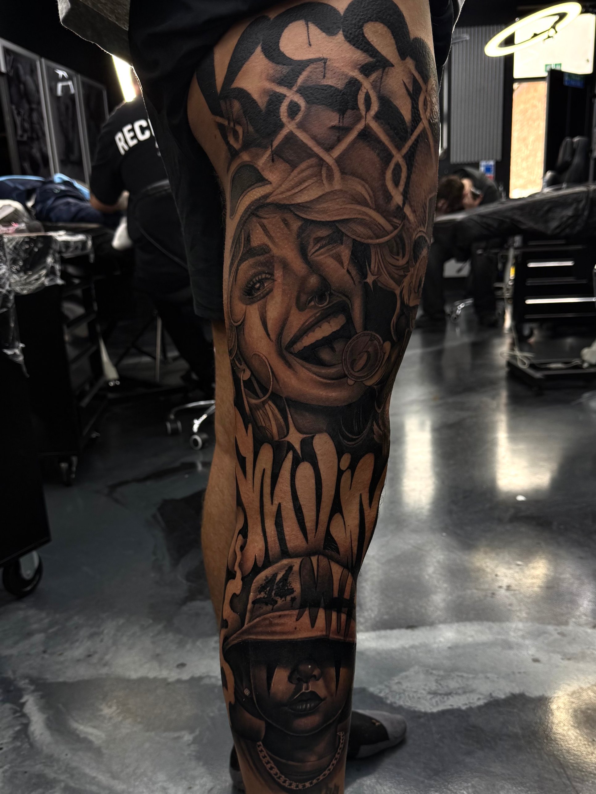 Black and grey clown portrait and graffiti lettering leg sleeve tattoo by Kayley Laroche at SANS PATRIE/ STUDIO