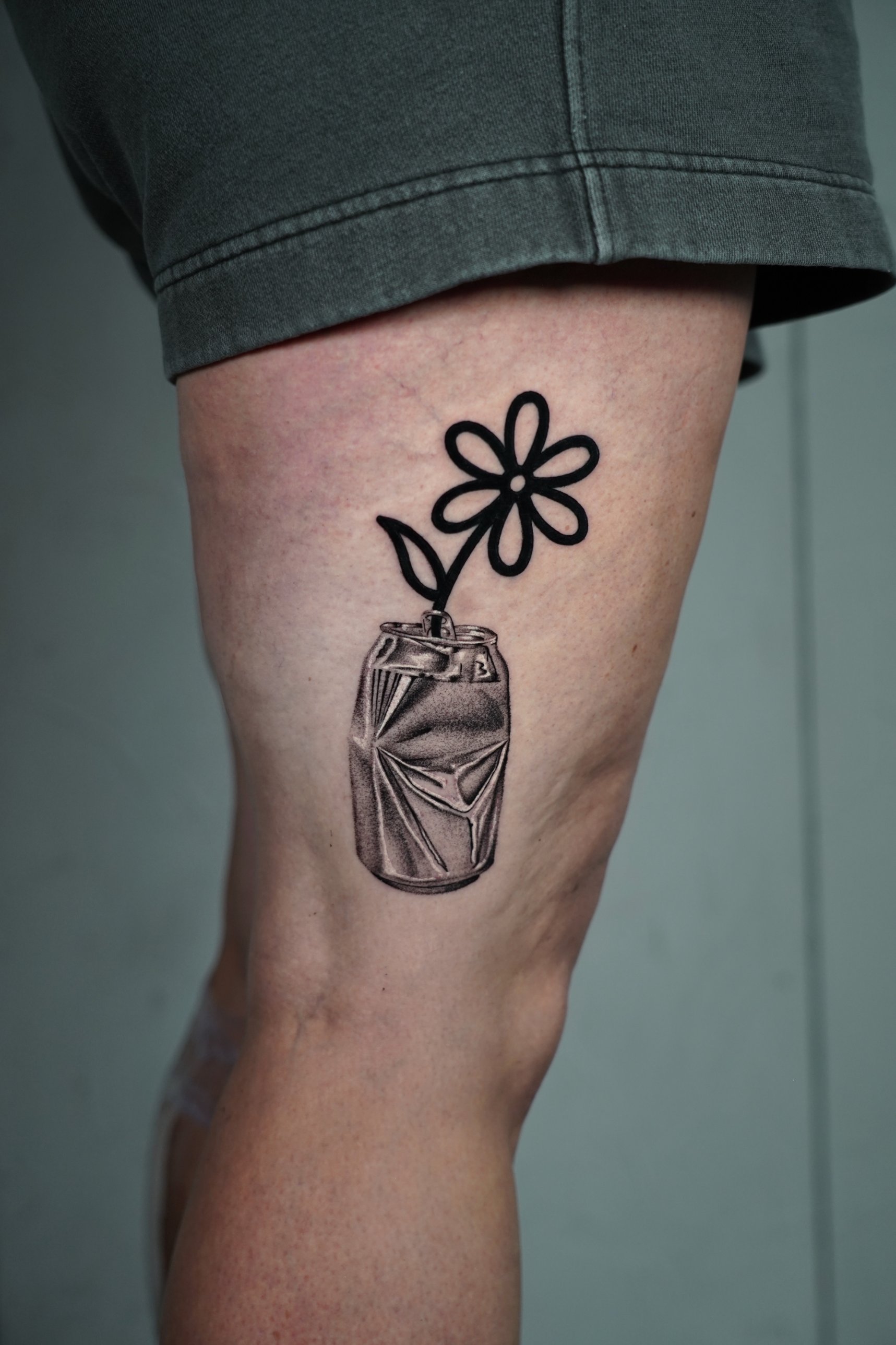 Black and grey crushed can with a bold outline flower thigh tattoo by Tommy Burley at SANS PATRIE/ STUDIO