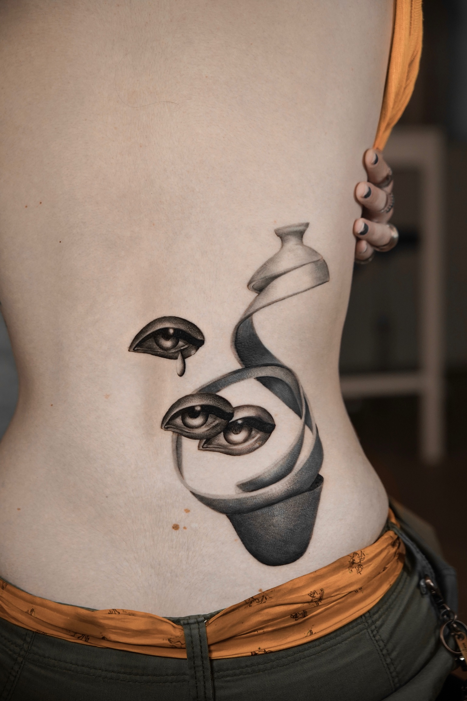 Black and grey surrealist eyes and spiralling vase lower back tattoo by Kimberley Verana at SANS PATRIE/ STUDIO