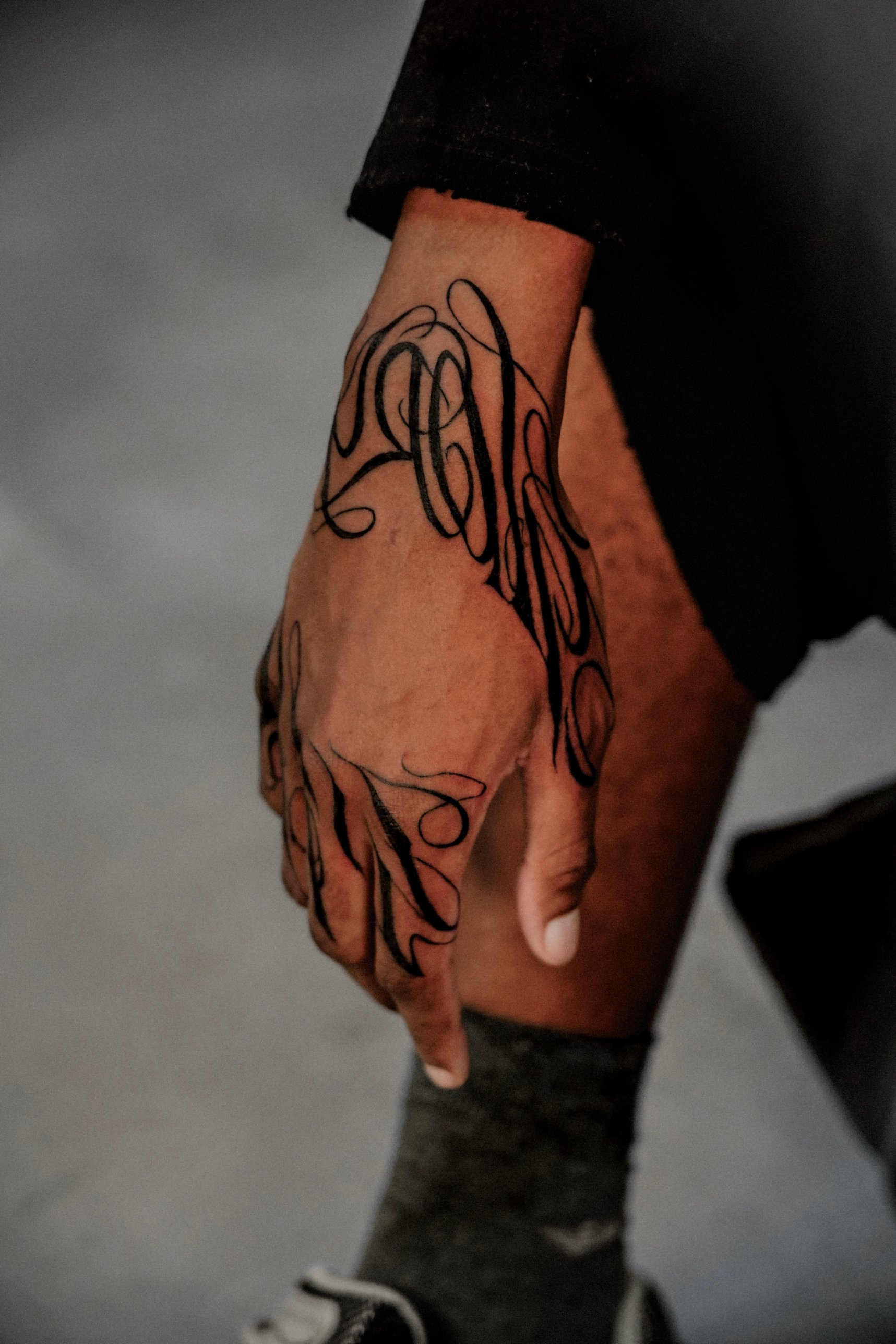 Flowing black script lettering hand tattoo by Kimberley Verana at SANS PATRIE/ STUDIO