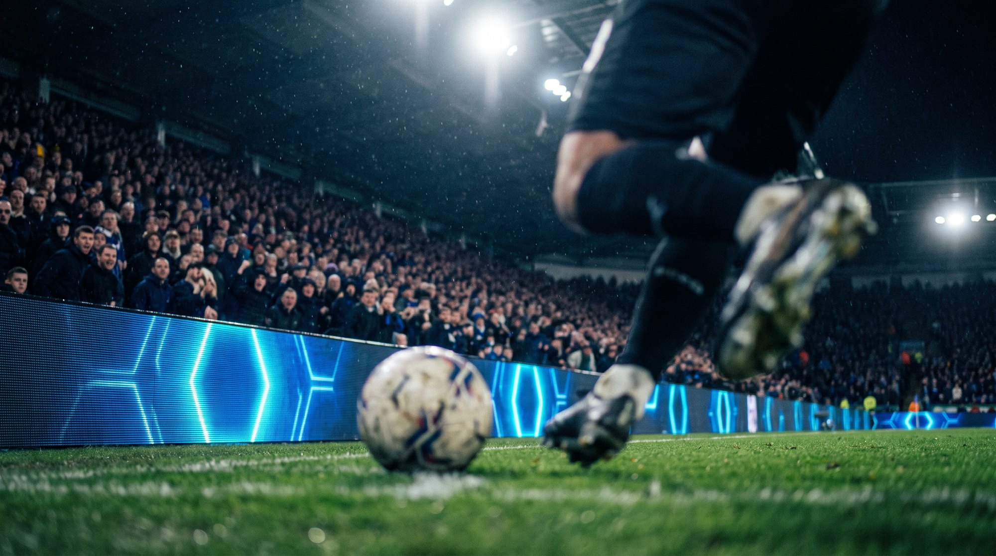 Soccer player lining up a free kick in front of illuminated stadium LED advertising boards.