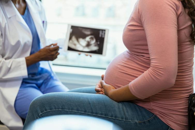 Pregnant person talks with medical professional with ultrasound image in background