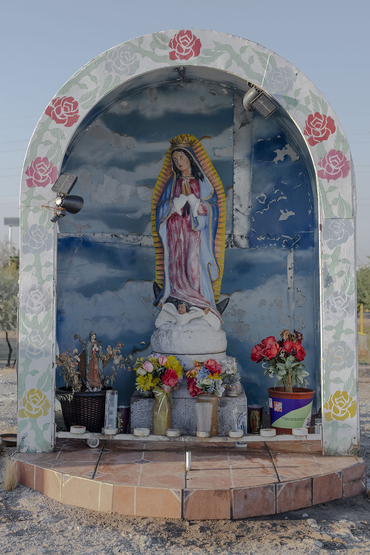 A painted statue of Our Lady of Guadalupe displayed in a decorative niche surrounded by flowers and candles.