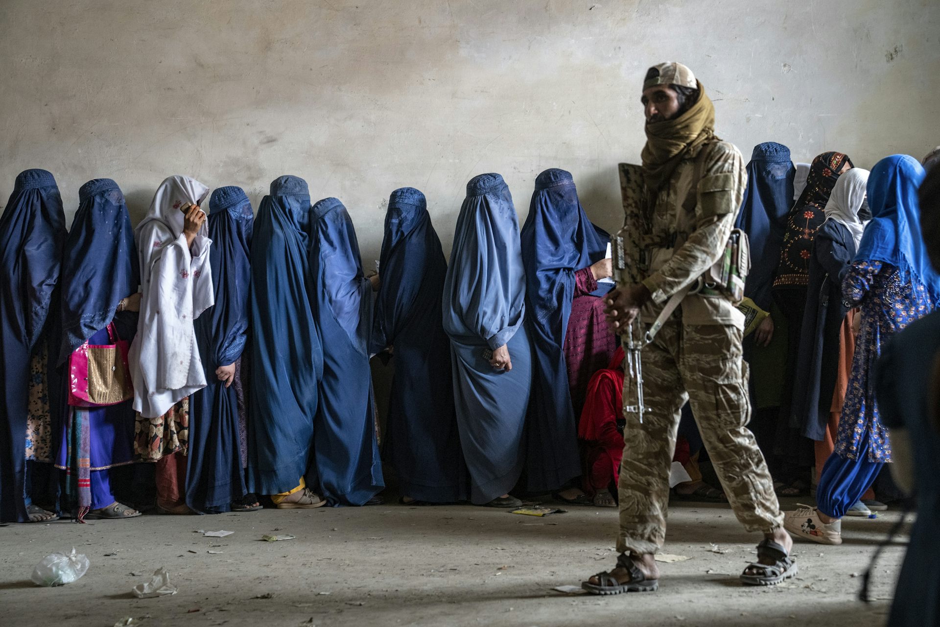 A Taliban fighter stands guard as women wait for food rations in Kabul