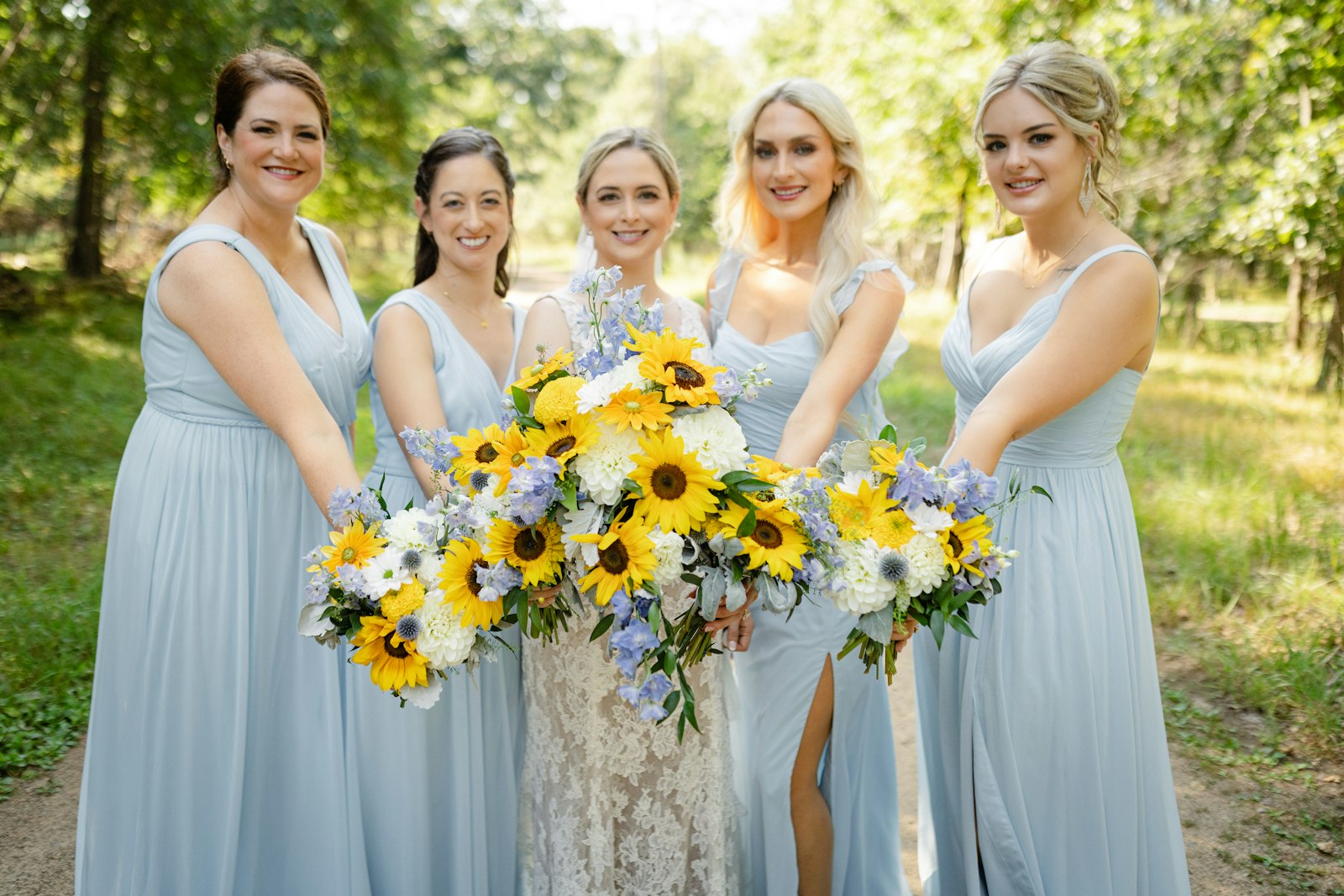 A smiling bride and her bridesmaids holding sunflower bouquets before the ceremony